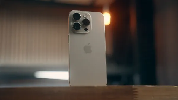 Một chiếc iPhone 15 Pro màu đen titan đặt trên mặt bàn, bên cạnh là hộp đựng và cáp sạc