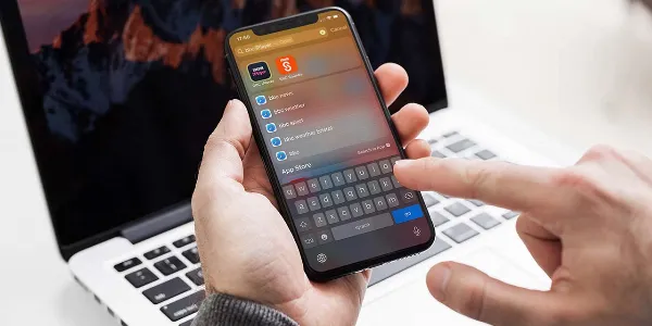 Một chiếc điện thoại iPhone đang hiển thị giao diện Spotlight Search với nhiều kết quả tìm kiếm khác nhau