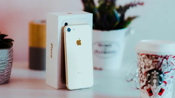 Một chiếc điện thoại iPhone màu đen đang được cầm trên tay, hiển thị màn hình cài đặt với nhiều tùy chọn khác nhau