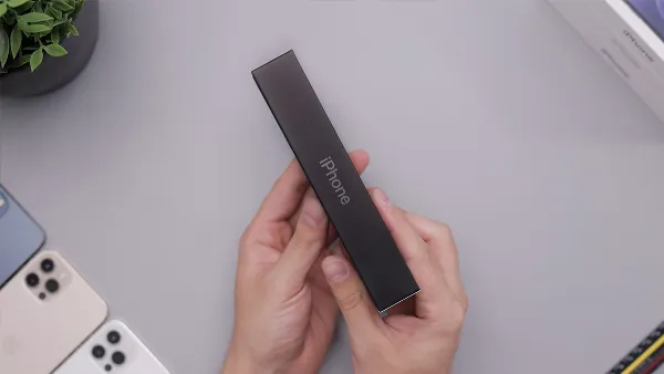 Một chiếc điện thoại iPhone màu trắng đang được cầm trên tay, hiển thị màn hình với biểu tượng sóng di động và dòng chữ GSM