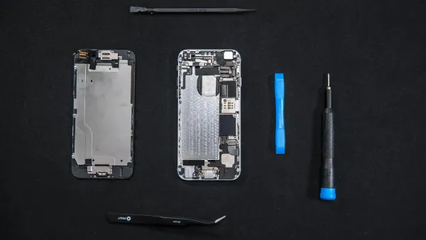 Một kỹ thuật viên đang sử dụng kính lúp và nhíp để sửa chữa bảng mạch của một chiếc điện thoại